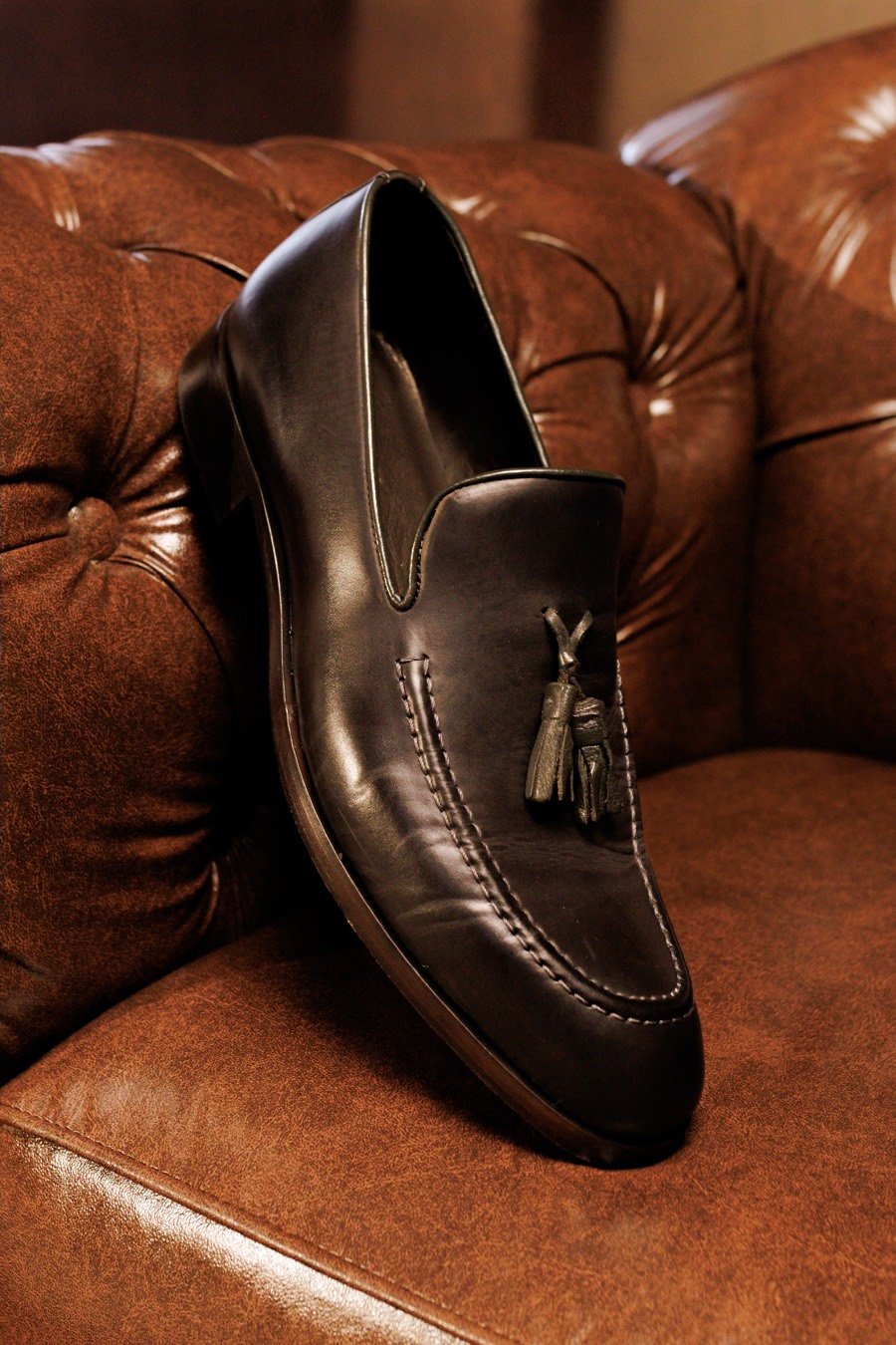 Loafer masculino de couro preto com franjas sobre poltrona de couro